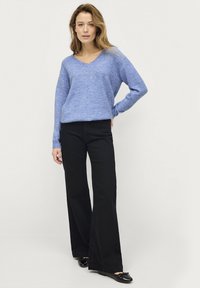Hellblauer, gestrickter V-Ausschnitt-Pullover mit langen Ärmeln, kombiniert mit hochtaillierten, schwarzen, ausgestellten Hosen und schwarzen Ballerinas. Einfaches und lässiges Design.