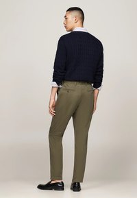 Maglione di lana a trecce blu navy sopra una camicia a righe chiara, abbinato a pantaloni verde oliva e mocassini neri, mostratto da dietro.