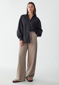 Black button-up shirt with long, billowy sleeves, paired with beige wide-leg trousers and black sandals. Smooth texture, simple design.