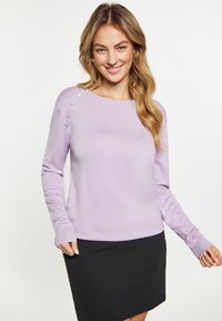 Maglione a maniche lunghe di colore lavanda con scollatura rotonda, caratterizzato da bottoni decorativi sulla spalla, abbinato a una gonna nera. Texture liscia.