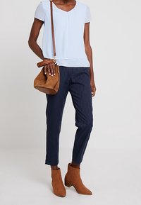Light blue short-sleeve blouse with a round neckline, paired with navy pinstripe trousers, brown suede ankle boots, and a brown leather bag.
