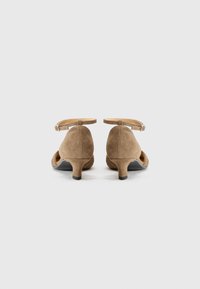 Chaussures à talons hauts en daim tan avec un bout rond, une bride à la cheville et un talon de hauteur intermédiaire. Texture lisse et design minimaliste.