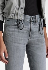 Jeans de mezclilla gris con corte slim, que cuentan con una cintura alta, bolsillos frontales y cordones ajustables negros en la cintura.