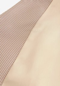 Tissu avec un tissu nude lisse et pâle à côté d'un motif en grille texturé marron et blanc, mettant en avant des matériaux et des surfaces contrastés.