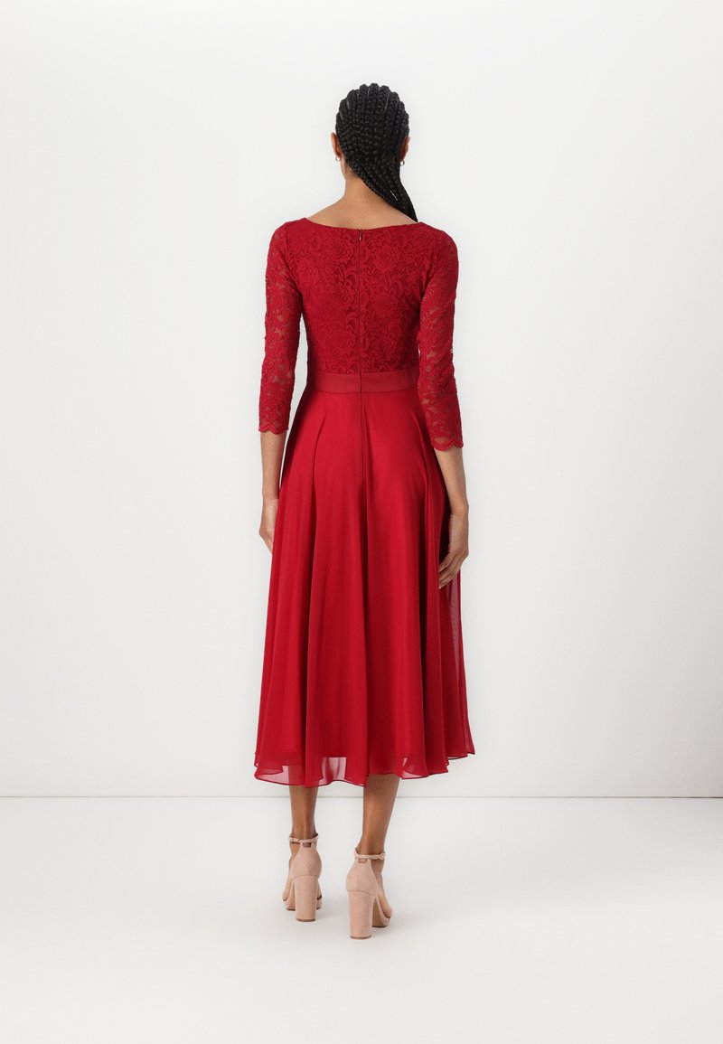 Rotes Kleid mit einem Spitzenoberteil, dreiviertel Ärmeln und einem fließenden Chiffonrock. Abgerundet mit nuden High Heels.