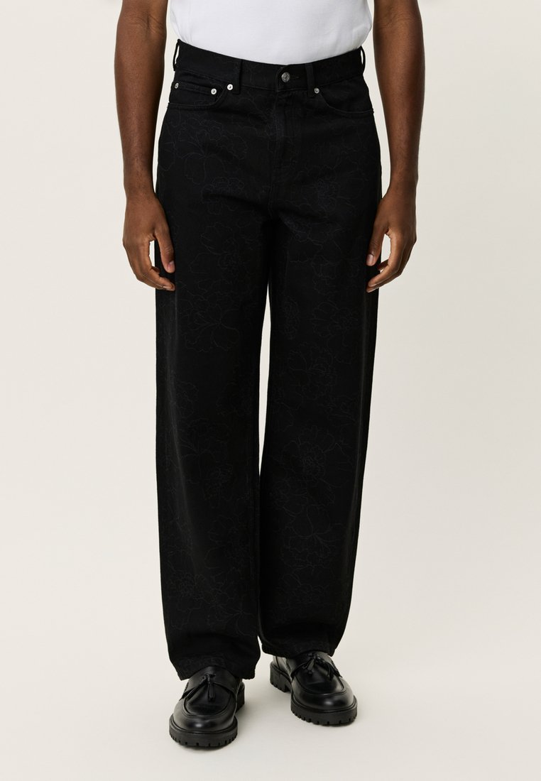 Μαύρο παντελόνι φαρδιάς γραμμής με ανάγλυφο λουλουδάτο σχέδιο, ψηλή μέση, σχέδιο με πέντε τσέπες, μεταλλικά εξαρτήματα και σε συνδυασμό με μαύρα παπούτσια.