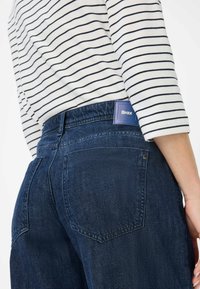 Dunkelblaue Jeans aus Denim mit einem gewebten Design, das eine geflochtene Textur aufweist, zwei Gesäßtaschen und einem rechteckigen blauen Markenlabel an der Taille.