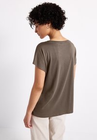Top de manga corta, color verde oliva, hecho de un material suave, con un corte relajado y escote redondeado, combinado con pantalones color blanco roto.