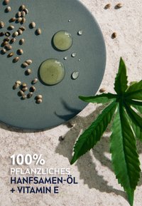 Green hemp oil droplets on a matte gray circular surface, surrounded by hemp seeds and a green hemp leaf on a textured beige background.