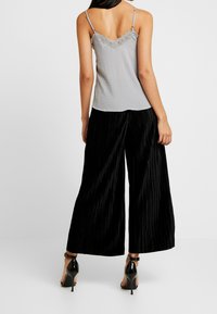 Canotta grigia con rifiniture in pizzo, abbinata a pantaloni neri a gamba larga con pieghe. L'outfit è completato da sandali neri con tacco alto.