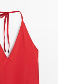 Haut rouge à col licou avec un profond décolleté en V et des fines bretelles nouées dans le dos, présenté sur fond blanc.