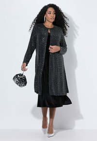 Cárdigan negro con embellishments brillantes, combinado con un vestido negro. También incluye un bolso negro texturizado y tacones plateados.
