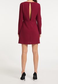 Bordeauxfarbenes Wollmischkleid mit langen Ärmeln, einem hohen Rückenteil und einem Schlüssel-ausschnitt. Verfügt über einen Reißverschluss auf der Rückseite.