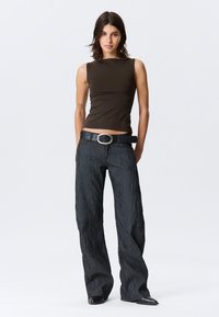 Καφέ τοπ χωρίς μανίκια με εφαρμοστή σχεδίαση, συνδυασμένο με παντελόνι με φαρδιά μπατζάκια σε σκουρόχρωμη υφή και μαύρη ζώνη με στρογγυλή ασημένια πόρπη.