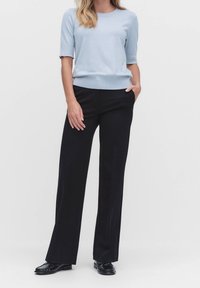 Světle modrý svetr s krátkými rukávy a žebrovaným lemem, kombinovaný s černými širokými kalhotami a černými botami, vytv�ářející ležérní outfit.