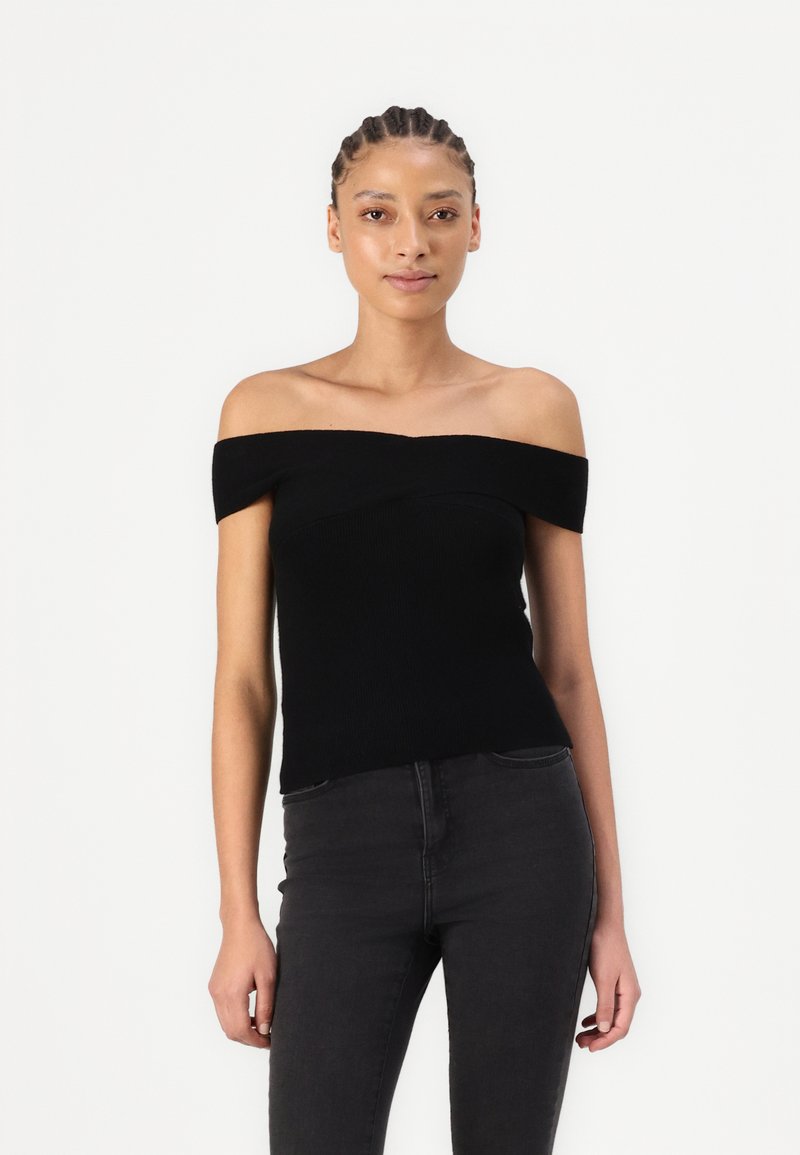 Juoda off-the-shoulder megztinis su trumpomis rankovėmis, prigludusia forma ir lygiu paviršiumi. Derinama su juodomis prigludusiomis džinsinėmis kelnėmis.