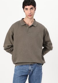 Khaki pullover with a classic collar, long sleeves, and a relaxed fit. Features a subtle logo on the left chest. Made from soft fabric.