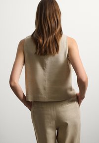 Top sans manches beige en tissu lisse et légèrement texturé, présentant un design cropped et un ourlet droit, associé à un pantalon assorti.
