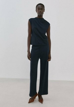 Costum bleumarin din două piese, compus dintr-un top fără mâneci și pantaloni largi, confecționat dintr-un material moale cu textură netedă. Pantofi cu toc maro și vârf ascuțit.