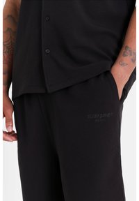 Chemise noire à boutons avec un tissu texturé, associée à un short noir arborant un logo en relief discret sur la poche avant.