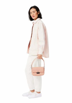 Sac à main en cuir rose avec un design structuré et une bandoulière amovible. Veste en denim blanche sur un haut marron, associée à des baskets blanches.