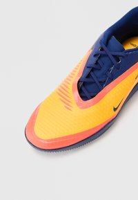Nike hardloopschoen met een verloop van felgeel naar oranje, voorzien van gestructureerde patronen, blauwe veters en een donkerblauwe basis.