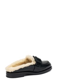 Scarpa nera in pelle slip-on con morbida fodera in pelliccia crema, punta rotonda e dettaglio decorativo sulla cinghia. Suola a profilo basso.