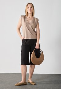 Top sin mangas beige, pantalones cortos cargo negros, zapatos planos color marrón claro y un bolso curvado marrón. Tela suave en la parte superior, estilo casual, detalles prácticos.