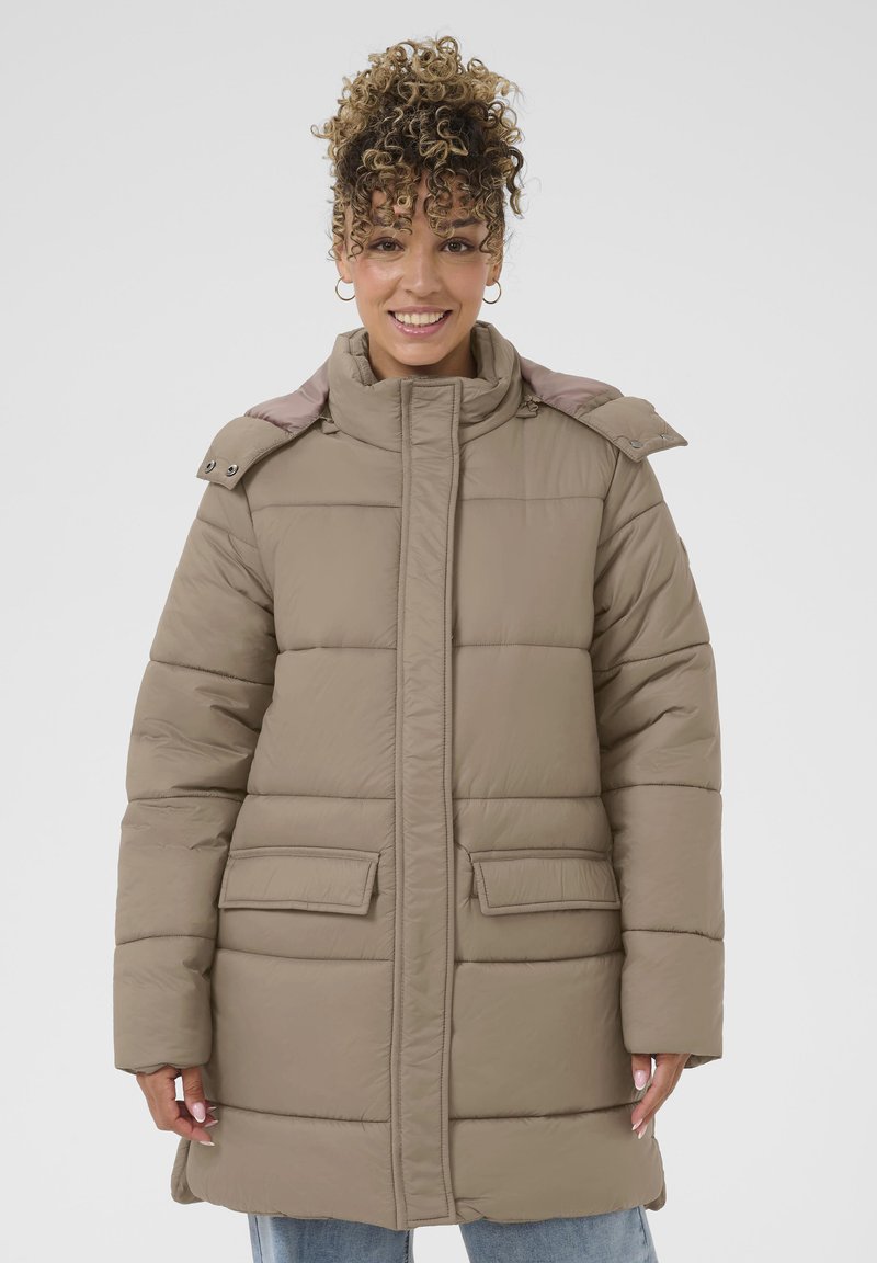 Beige polstret jakke med høj krave, trykknapdetaljer og to forlommer. Har et quiltet design og en glat tekstur.