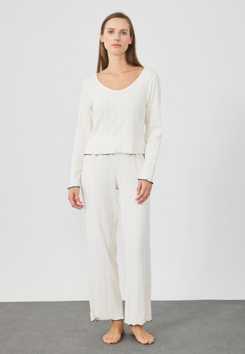 Ensemble de pyjama en tricot couleur crème comprenant un haut à manches longues en V, des bords festonnés et un pantalon à jambes larges, avec un motif texturé en ribbed.