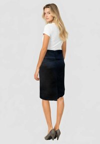 Falda lápiz negra texturizada con una cinturilla ancha, combinada con una camiseta blanca ajustada y zapatos de tacón altos grises.