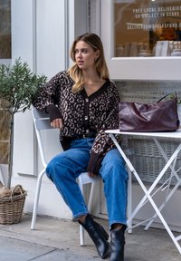 Brown and beige leopard-print sweater, high-waisted blue jeans, and black ankle boots, with a burgundy leather bag on a white table.