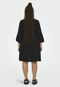 Black knee-length dress with three-quarter sleeves, lightweight textured fabric, and a loose fit. Features a back vent for ease of movement.
