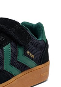 Sneaker nera in suede e rete con accenti verdi e design a righe, dotata di suola in gomma beige e strap in velcro per la chiusura.
