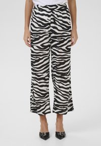 Fekete-fehér zebra mintás nadrág, rugalmas derékkal, széles lábakkal és oldalsó sliccekkel az alján. Matt textúra.