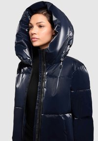 Námořnická puffer bunda s podšívkou a lesklým povrchem, s přehnanou kapucí a předním zipem. Disponuje prošívaným švem a elegantním, moderním designem.