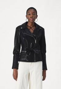 Giubbotto in finta pelle nera con design aderente, chiusura con zip, vita con cintura, dettagli a costine su maniche e spalle e finitura lucida.