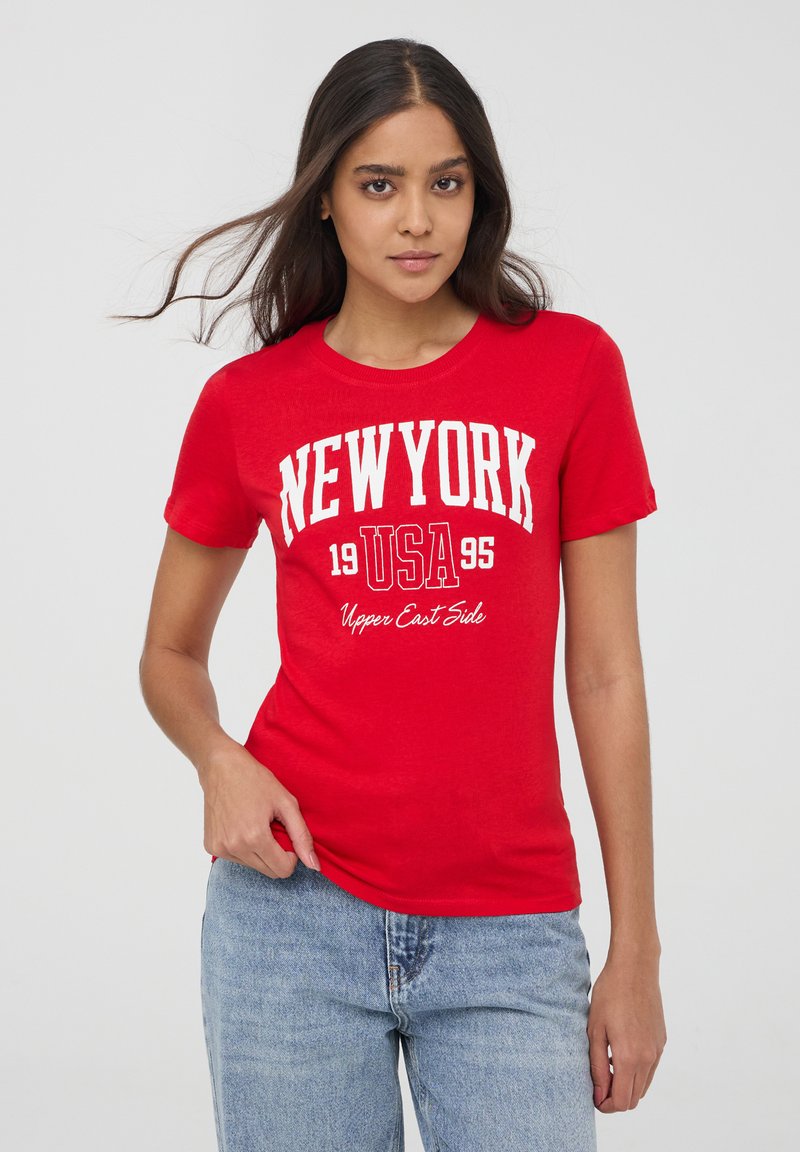 T-shirt in cotone rosso con maniche corte, con stampa bianca che recita: "NEW YORK 1995 USA Upper East Side." Vestibilità casual con colletto a girocollo.