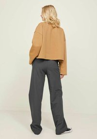 Bruine oversized cropped sweatshirt in combinatie met grijze wijde broek. De outfit heeft een relaxte pasvorm en is gemaakt van zachte stof met een casual ontwerp.