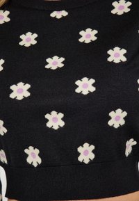 Maglione nero lavorato a maglia con un motivo floreale che presenta fiori bianchi con centri viola, design aderente e collo e orlo a coste.