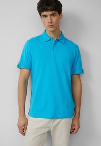Turkooise poloshirt van katoen, met een klassieke kraag, korte mouwen met opgerolde mouwen en een subtiele textuur.