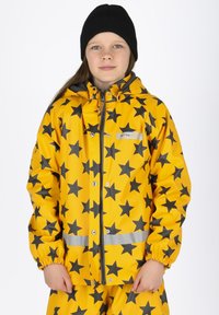 Gele regenjas met zwart sterrenpatroon. Voorzien van elastische manchetten, reflecterende strips en een rits aan de voorkant. Gecombineerd met bijpassende broek.