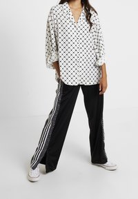 Camicia bianca con un motivo a rombi neri. Pantaloni neri con strisce bianche verticali. Sneakers bianche completano l'outfit.