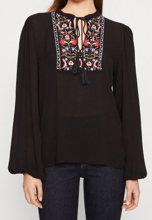 Blusa nera con maniche lunghe e voluminose. Presenta un collo a chiave con ricami floreali colorati e dettagli con frange lungo l'apertura.