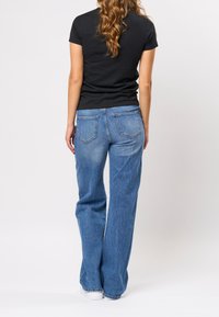 Modré džínové džíny s rovnými nohavicemi, vybavené klasickým designem s pěti kapsami, a tmavé tričko, pohled zezadu.