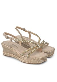 Beige wedge sandalen met een gestructureerde jute zool, voorzien van een strappy ontwerp versierd met goudkleurige details en verstelbare enkelbandjes.