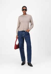 Maglione beige lavorato a maglia con dettaglio del logo, jeans blu a vita alta, stivali neri alla caviglia e una borsa rossa. Tessuto liscio e vestibilità comoda.