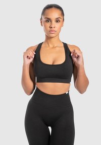 Schwarzes Sport-BH mit quadratischem Ausschnitt und breiten Trägern, kombiniert mit hochgeschnittenen schwarzen Leggings. Glatte Textur und taillierte Passform.