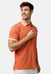 Pomarańczowa bawełniana koszulka polo z białymi paskami na kołnierzyku i rękawach. Slim fit, z prostym dołem i bocznymi rozporkami dla większej elastyczności.