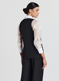 Schwarze maßgeschneiderte Weste mit durchsichtigen, hellen Ärmeln und einem weißen Kragen. Glattes Material mit minimalen Details. Seiten- und Rückansicht.